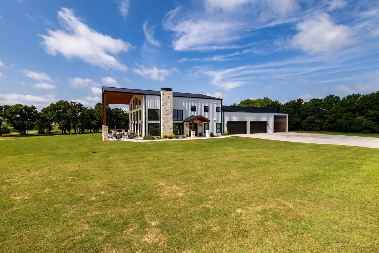 White metal barndominium with limestone accents and a timber-framed outdoor room