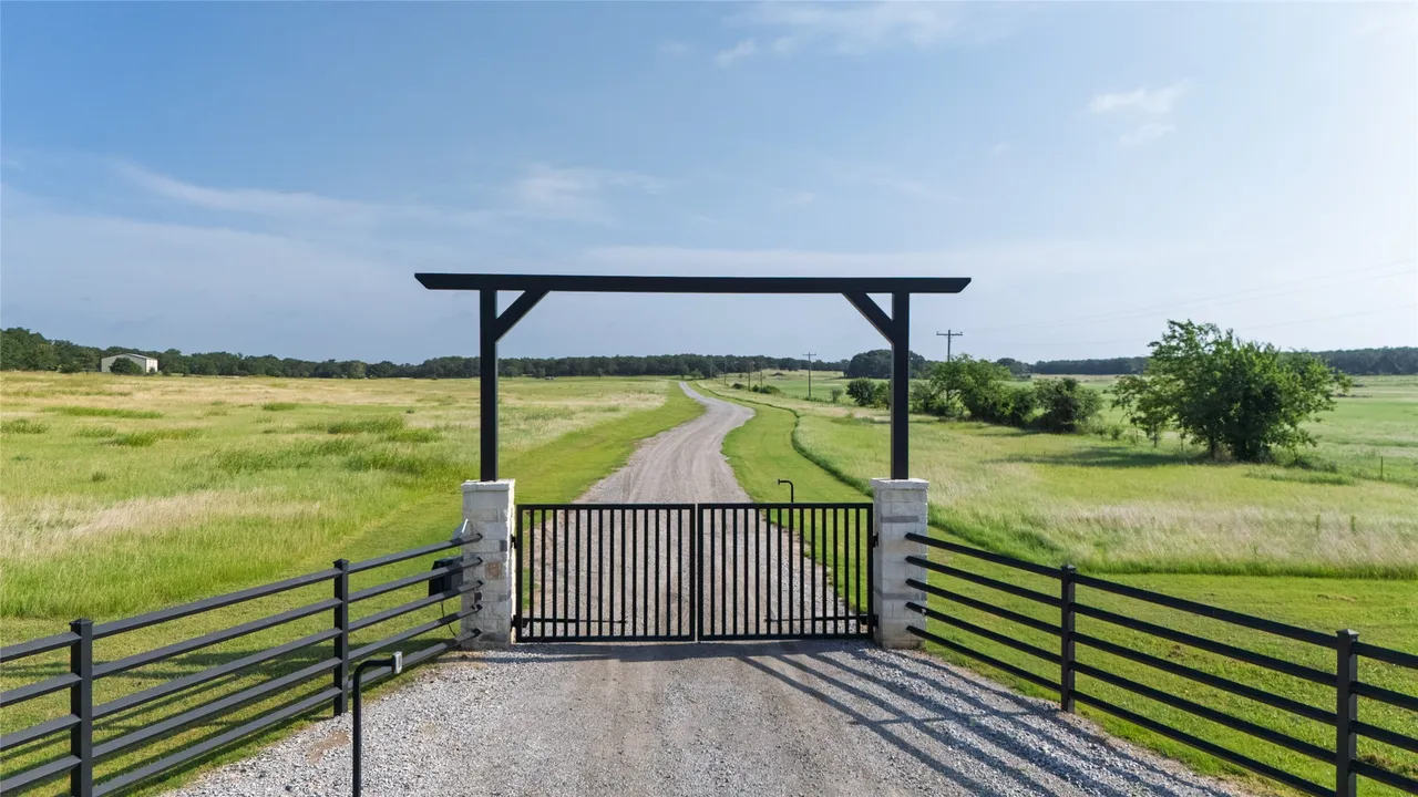 Black steel entry gate with limestone columns and pipe fencing