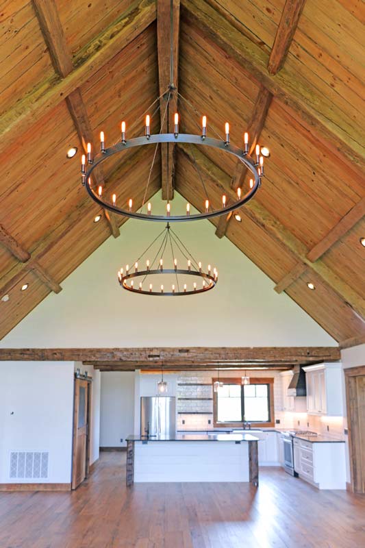 Rustic mountain ranch great room with vaulted plank ceiling, timber trusses and two iron ring chandeliers