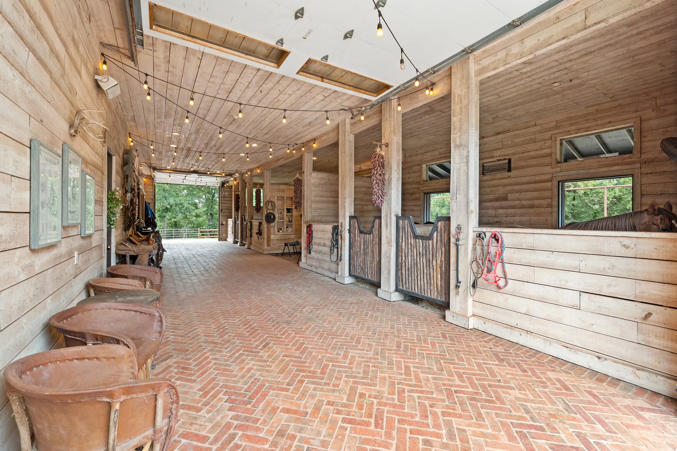 Barn center aisle with herringbone brick floor, weathered wood stalls and string lighting