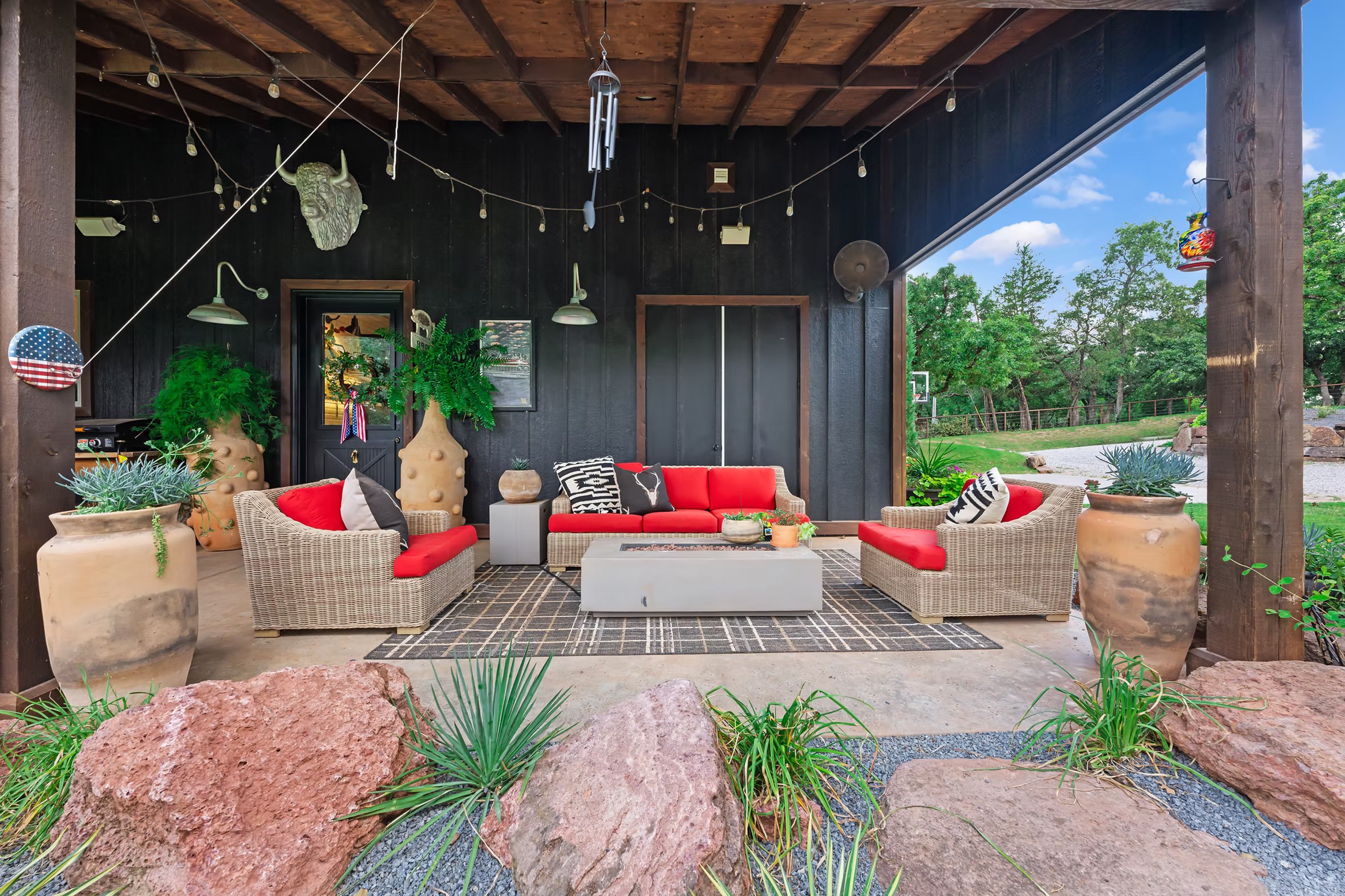 Covered ground level patio with woven furniture, red cushions and oversized pottery