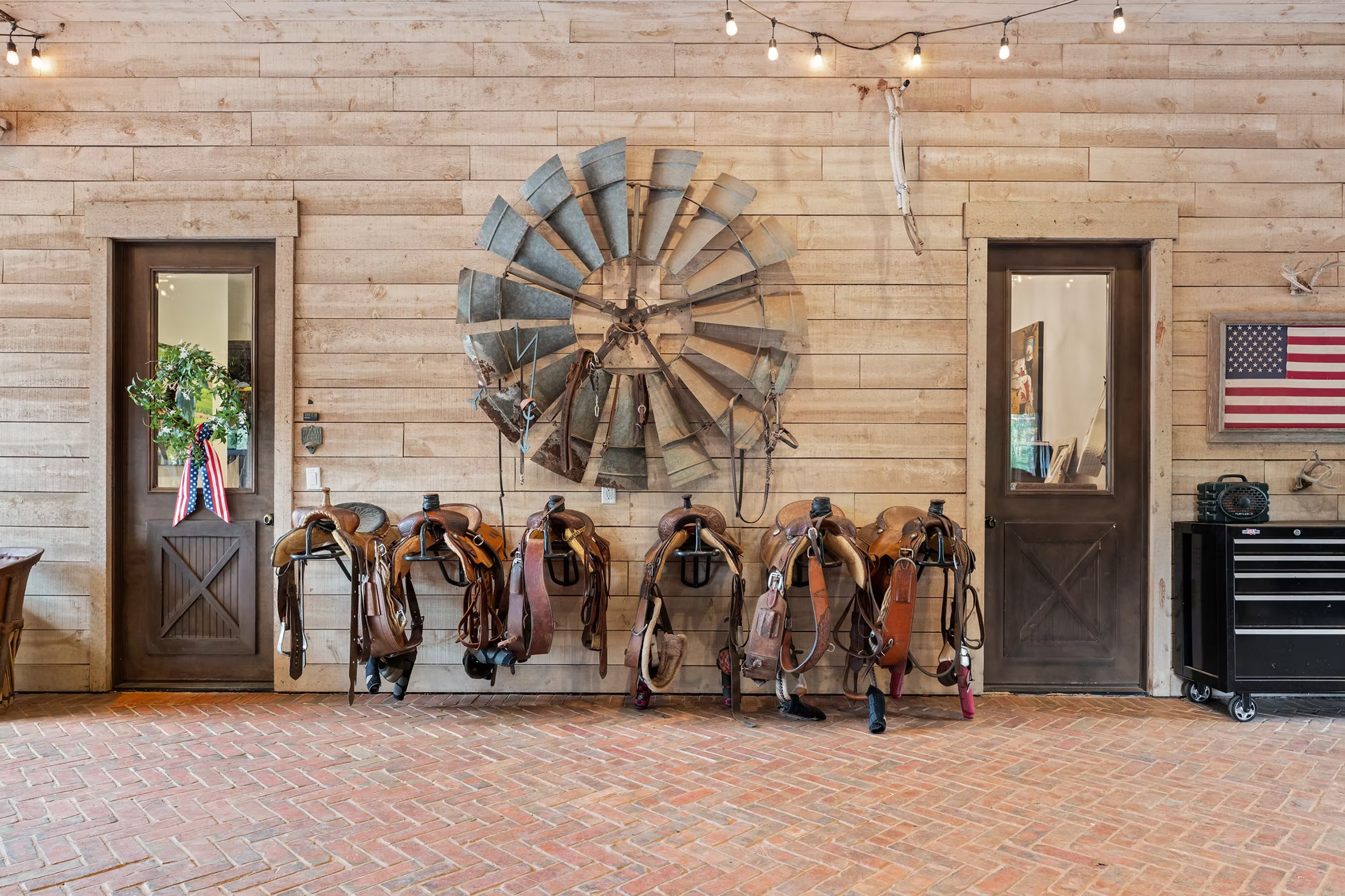 Saddles racked beneath an antique windmill blade mounted on the barn wall