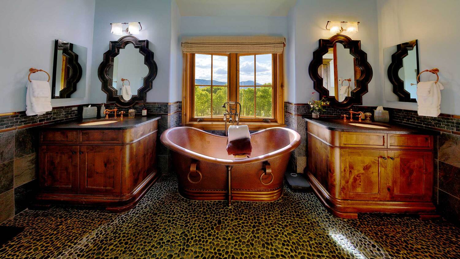Copper soaking tub beneath a window between two wood vanities and round mirrors at Eagle Ridge Ranch