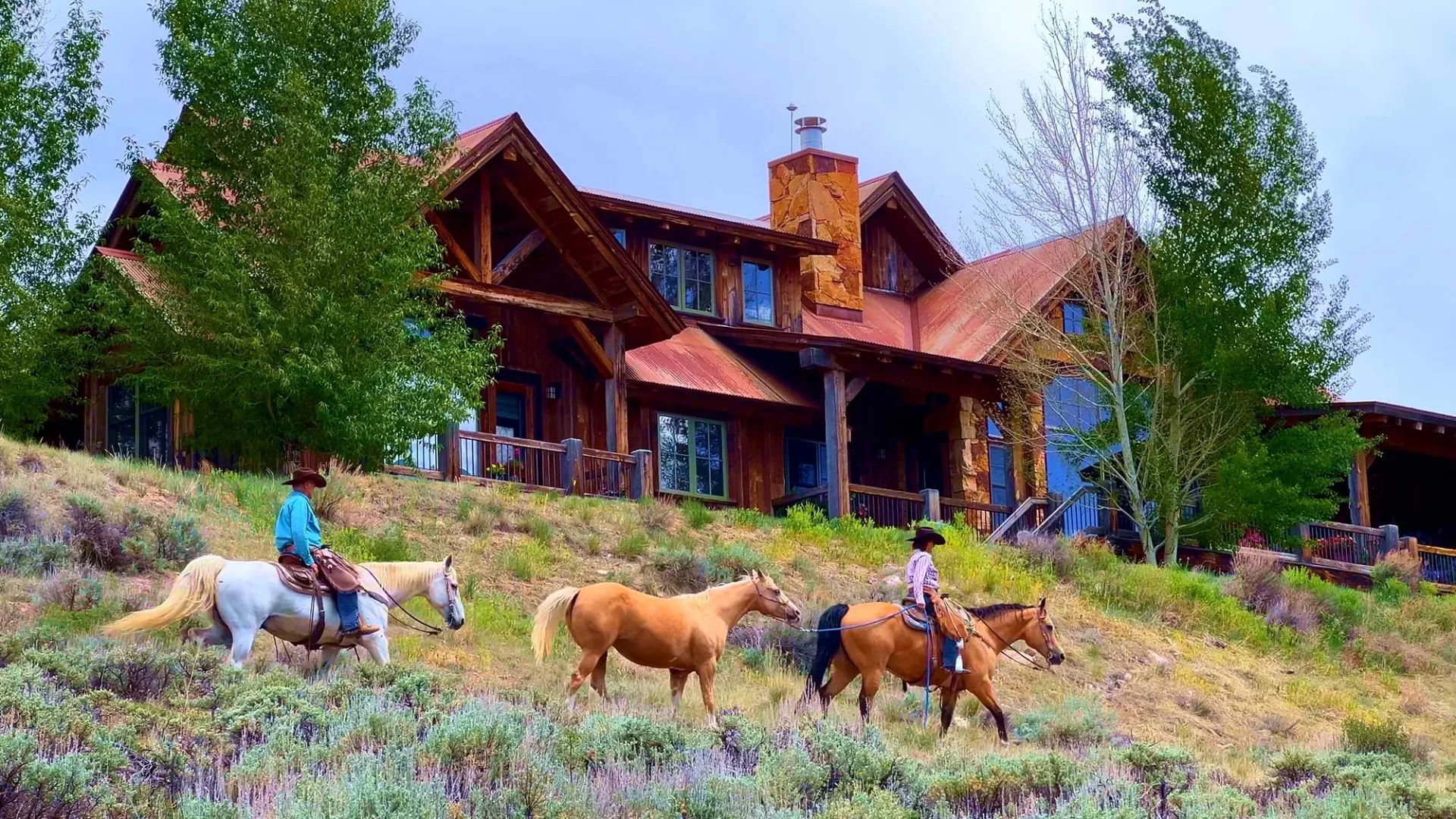 Riders on horseback passing the timber home at Eagle Ridge Ranch