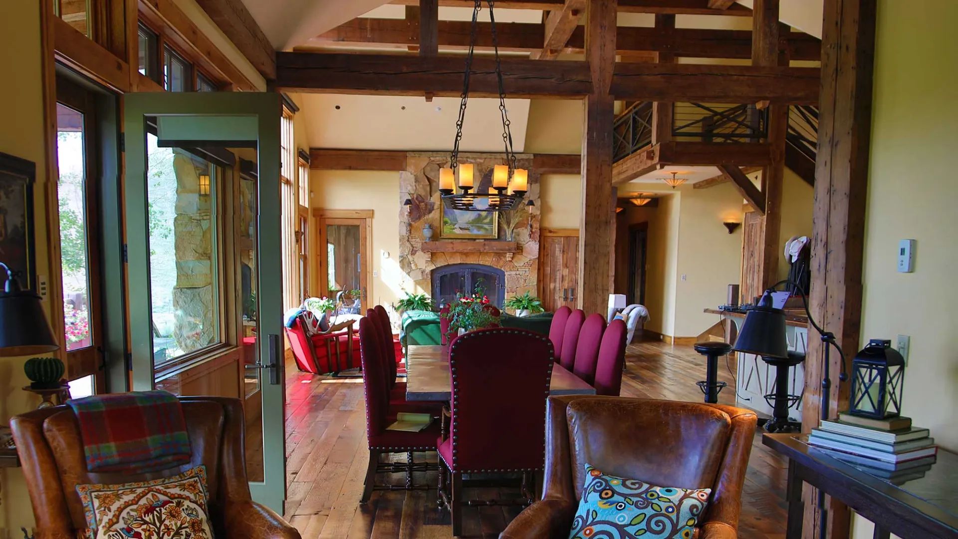View beneath the reclaimed timbers toward the dining table, chandelier and stone fireplace at Eagle Ridge Ranch
