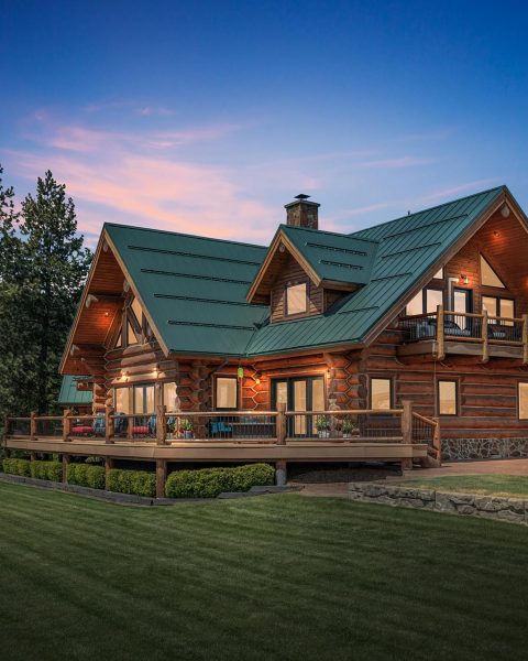 Custom log home at Painted Rose Ranch glowing at dusk above Lake Coeur d'Alene, Idaho